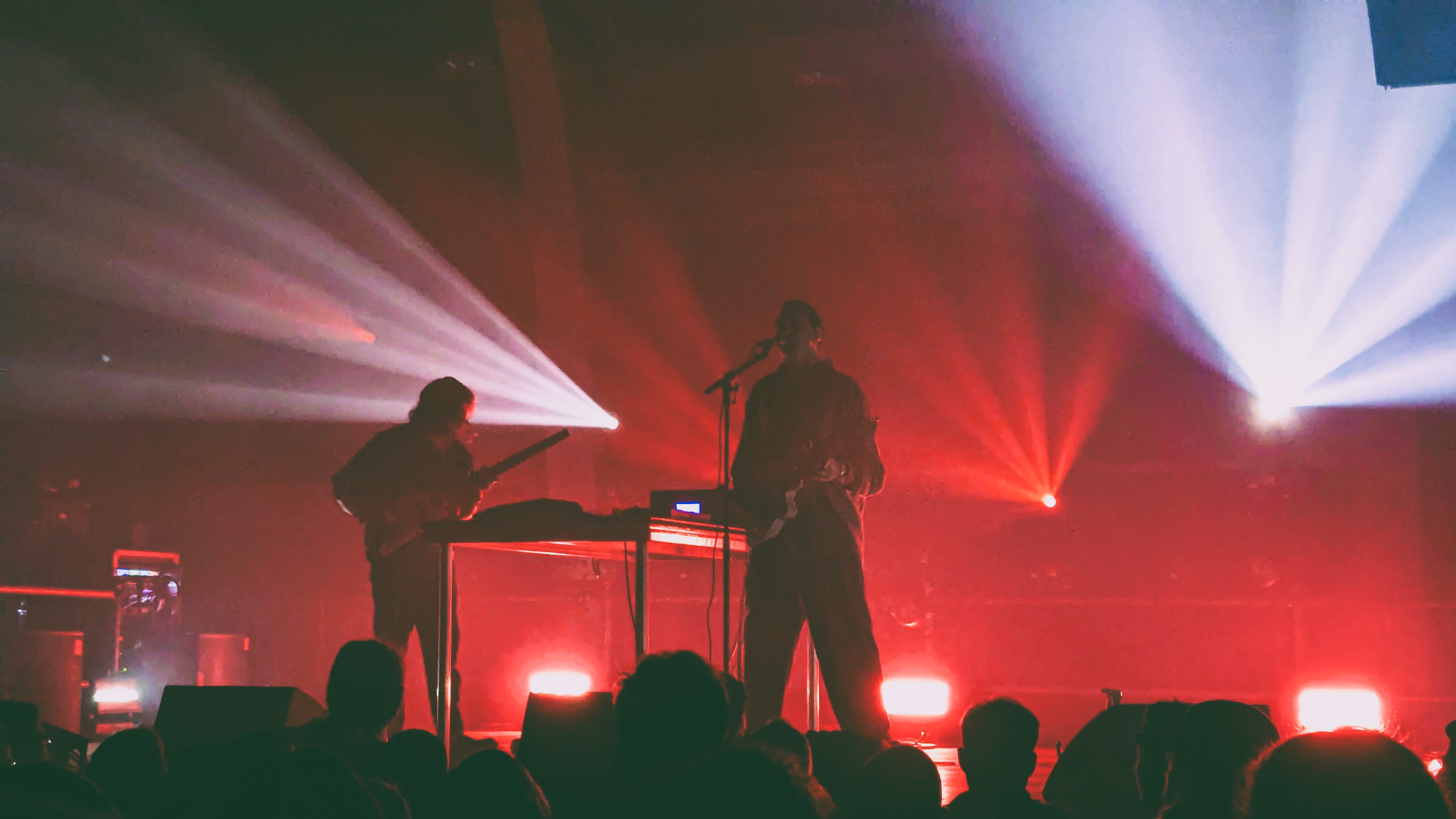 A live performance at a music festival featuring two musicians on stage with dramatic lighting effects, including red and white beams projecting from the background.