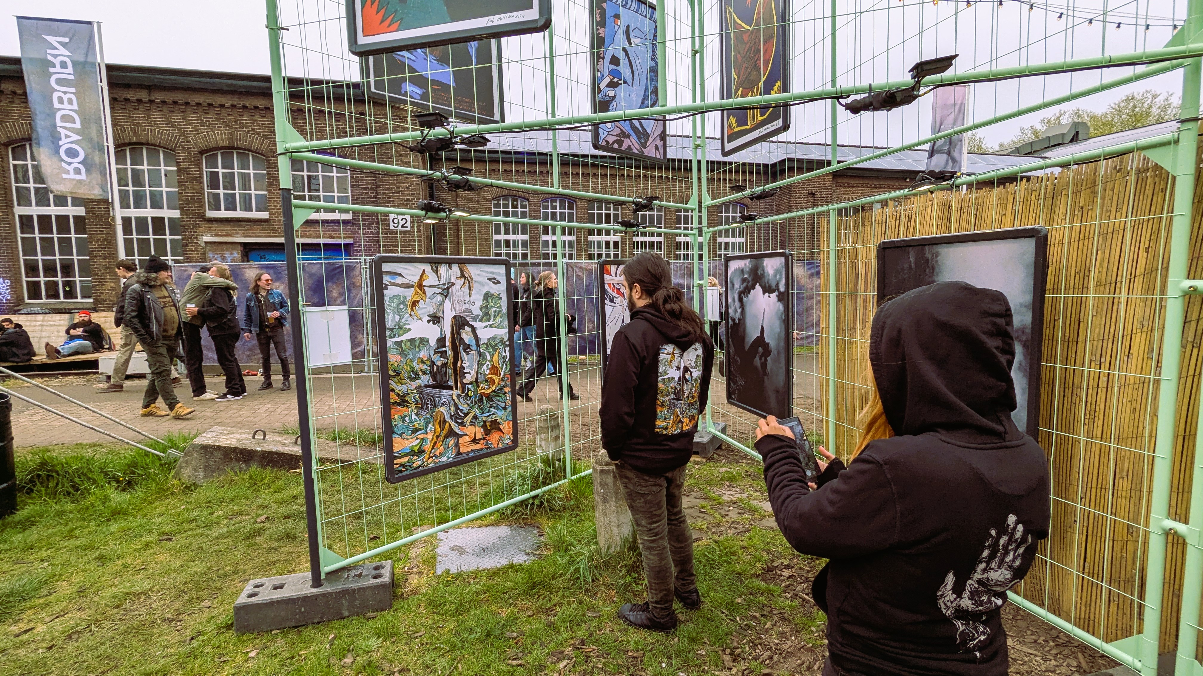 Attendees viewing artwork displayed at the Roadburn music festival, surrounded by a festival atmosphere with various posters and banners in the background.